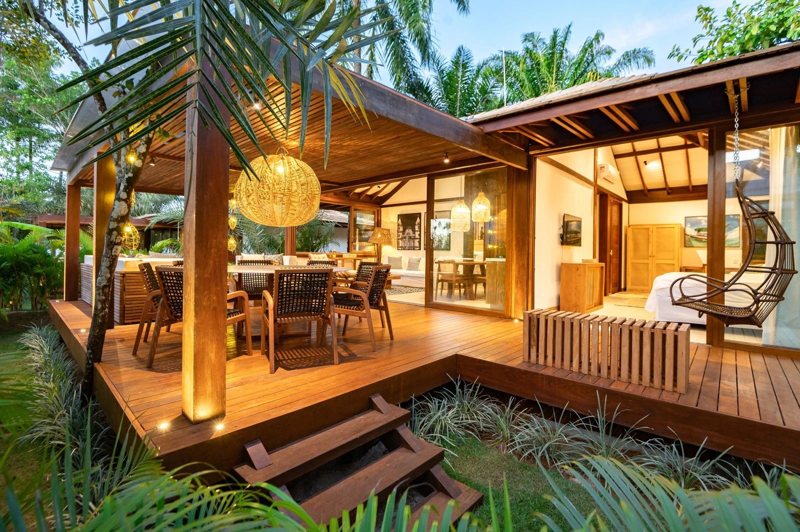 Villa do Colibri com varanda de madeira, jardim tropical e ambientes integrados iluminados