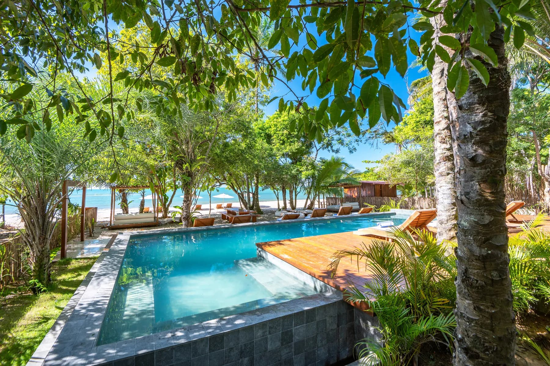 Piscina e deck do Colibri Beach Villas diante do jardim tropical